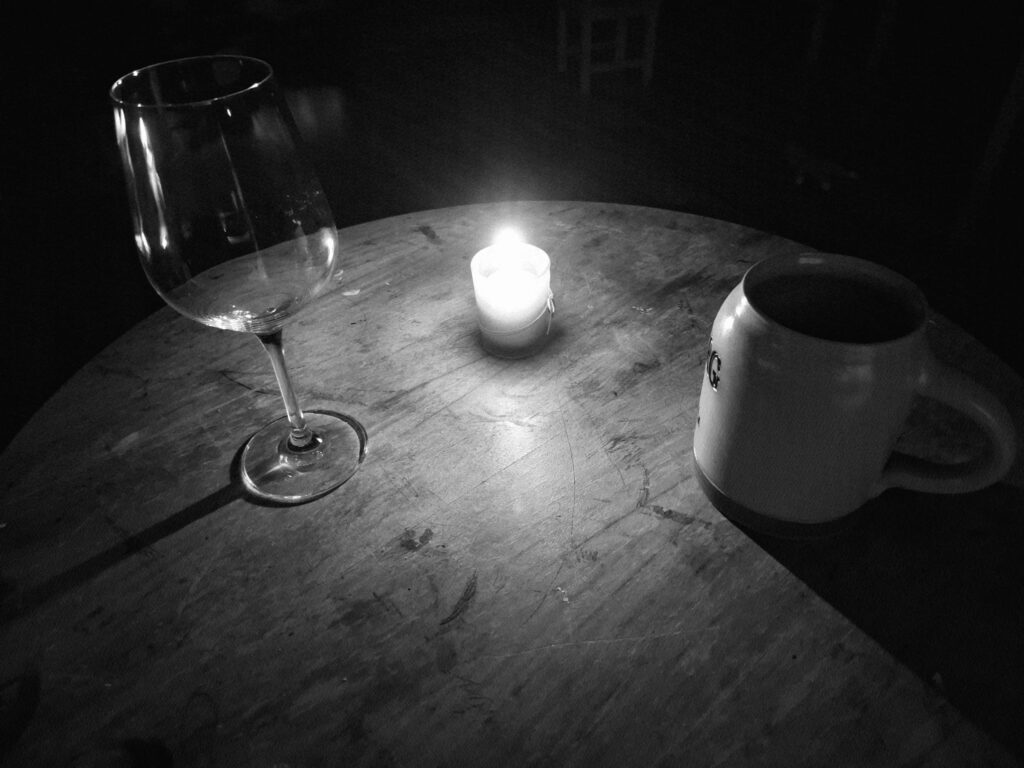 Ein alter Tisch, eine Kerze, ein Glas, ein Krug. Grimdark Fantasy Stimmung in Aethels Taverne. Schwarz weiß.
